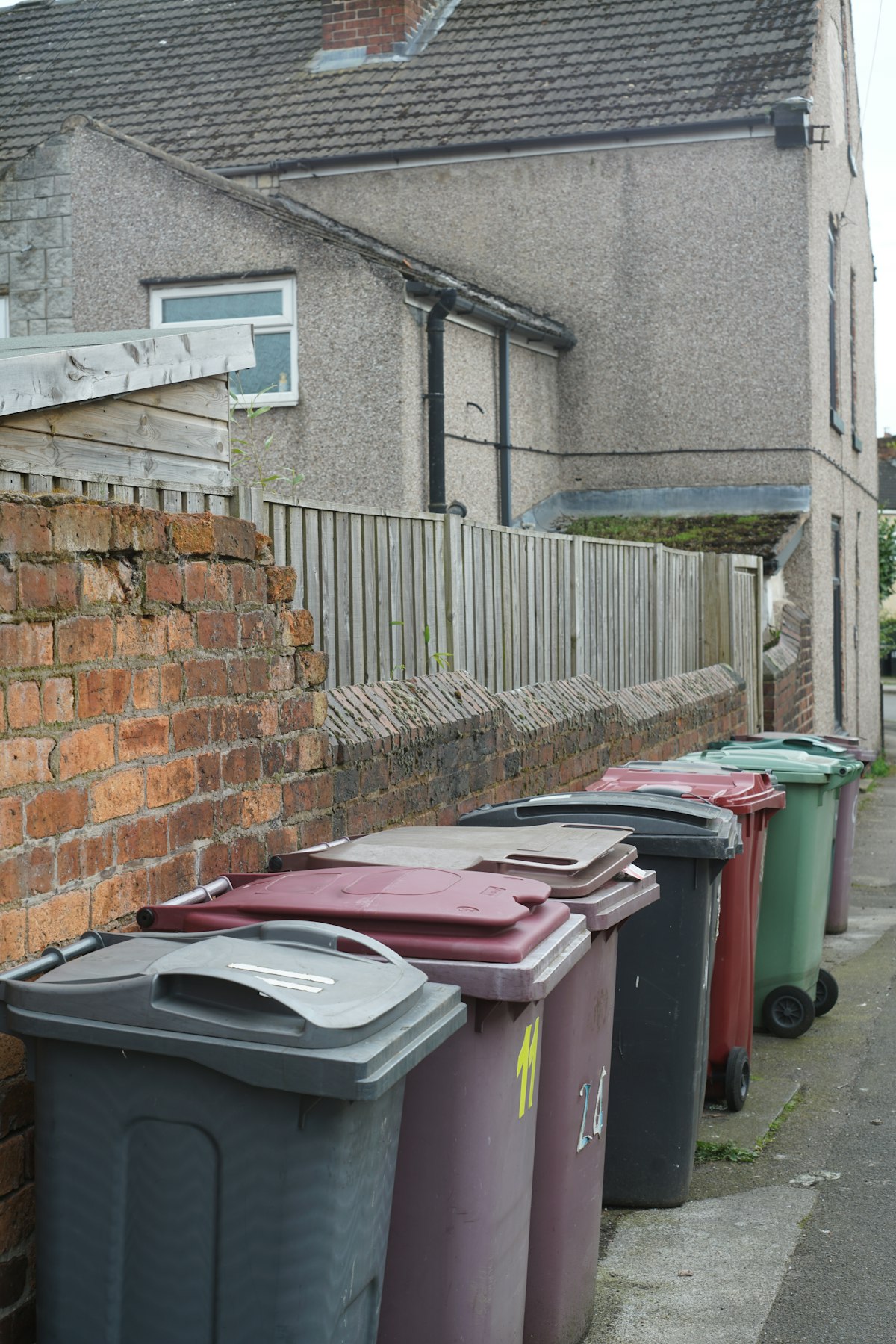 A row of wheelie bins against a brick wall